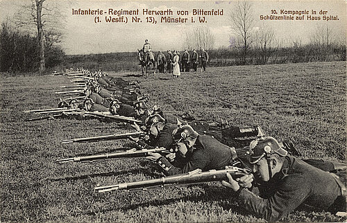 Schwarzweißfoto auf einer Postkarte. Soldaten liegen mit dem Gewehr zielend auf einer Wiese.