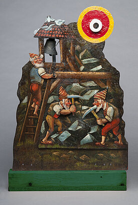 Ein Ziel der Schießhalle Schönhagen-Genert: Metallschild mit einer gemalten Darstellung von drei Zwergen in ihrer Miene. Einer schlägt eine Glocke. Neben der Glocke ist ein Zielfeld angebracht.